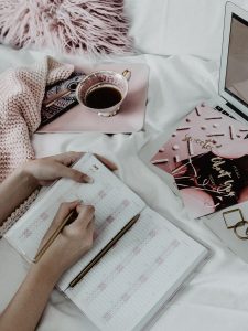 Pink and White Bed Flatlay for Instagram in minimal chic- Blonde Girl is writing in a calendar doing a coffee break by Be Sassique