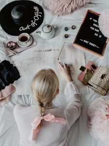 Pink and White Bed Flatlay for Travelinspo at Instagram in minimal chic- Blonde Girl lying in bed is looking at a map for the next vacation destination and all her travel dreams by Be Sassique